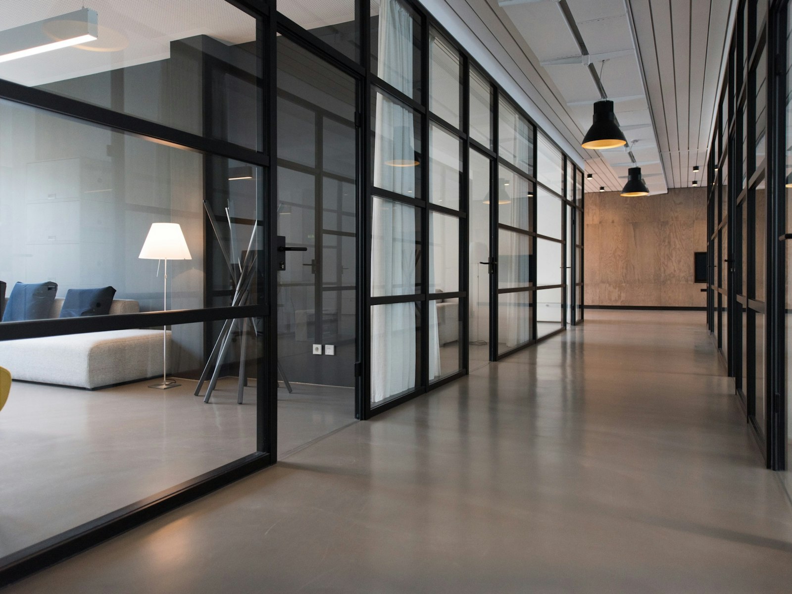 Modern office corridor with glass meeting rooms and a seating area